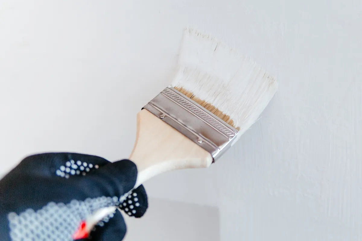 Gloved hand cutting in a white wall with a brush