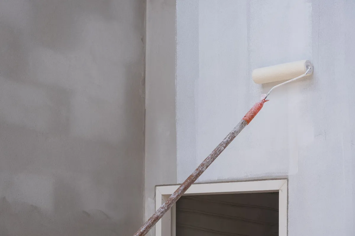 Extension roller painting a white interior wall beside a doorway