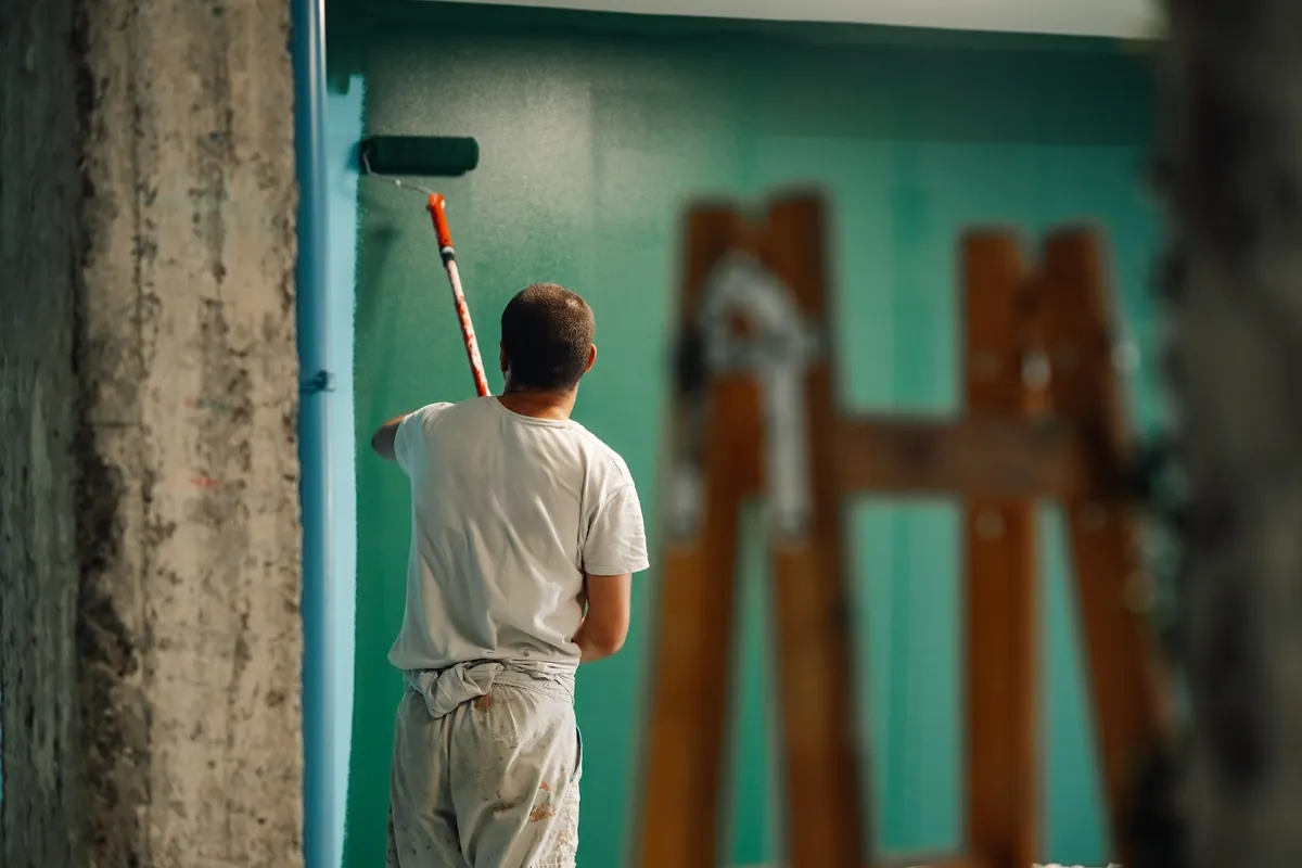 Painter rolling teal paint onto a wall
