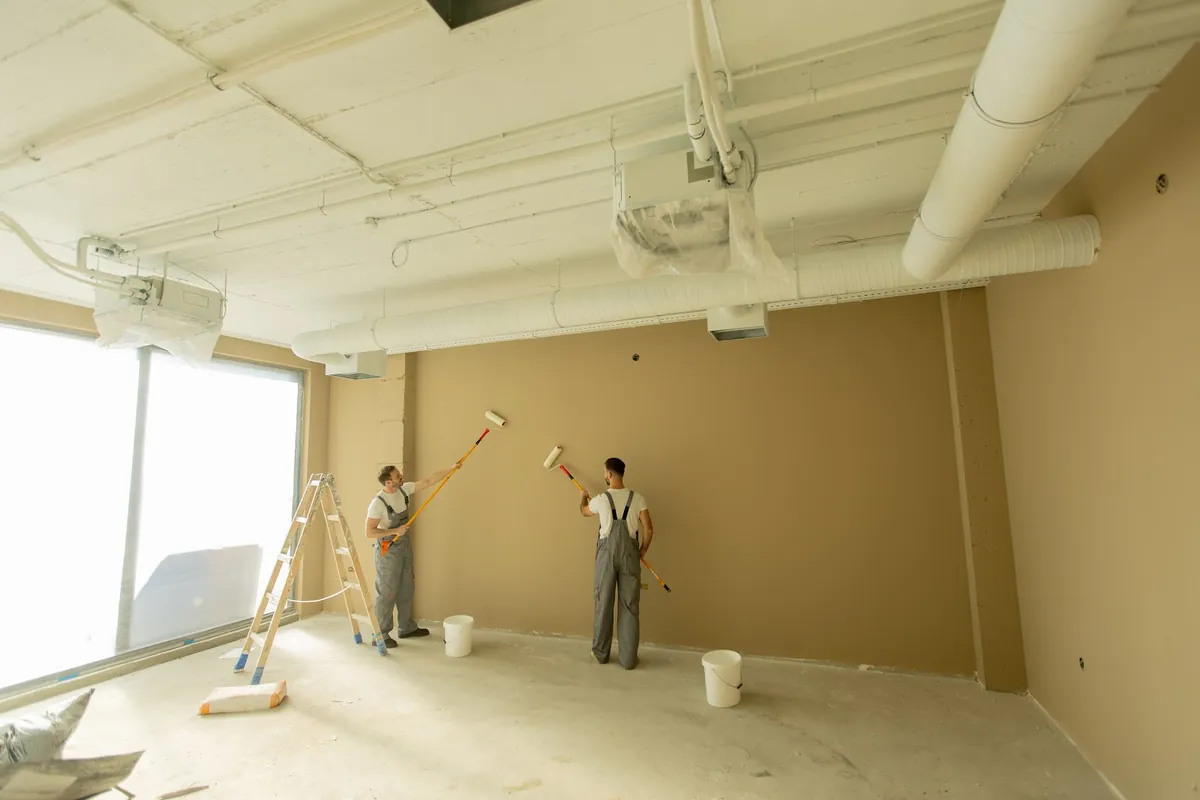 Two painters rolling paint onto the walls of an empty office