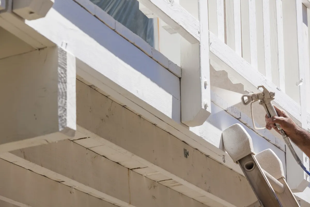 Painter spraying white paint on the underside of a raised deck